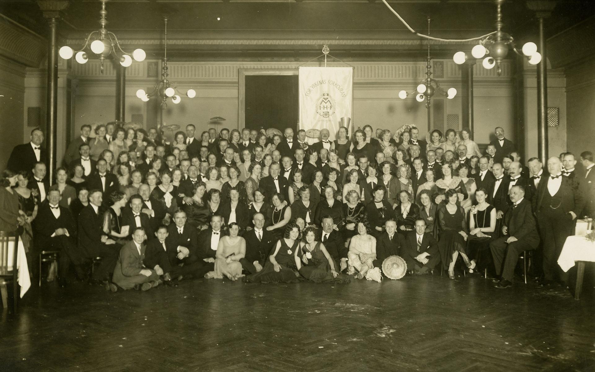 Foto från Hantverksföreningens tioårsjubileum 1935, med en lång rad finklädda damer och herrar. I bakgrunden syns föreningsfanan.